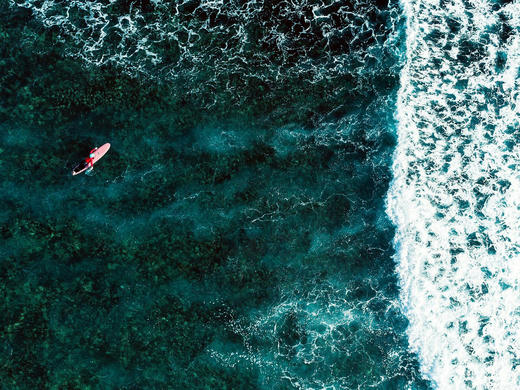 Aerial view of a surfer paddling out over the reef at Siargao